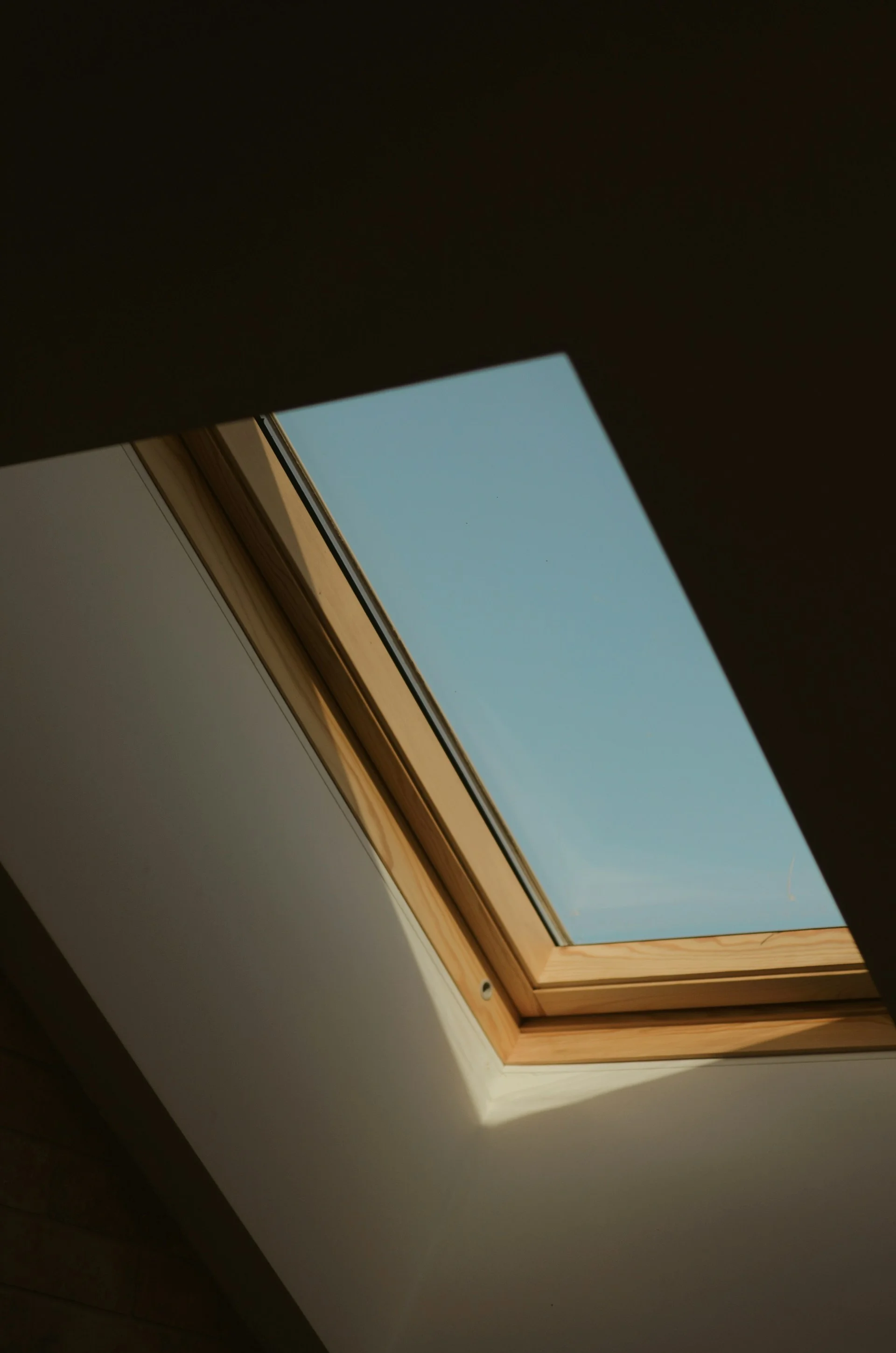 A residential skylight with a wooden VELUX-style frame mounted in a sloped attic ceiling